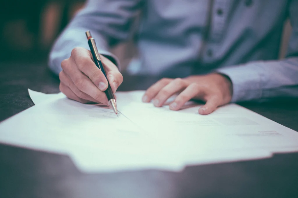 Person signing documents symbolizing how to flatten a PDF to make it uneditable.